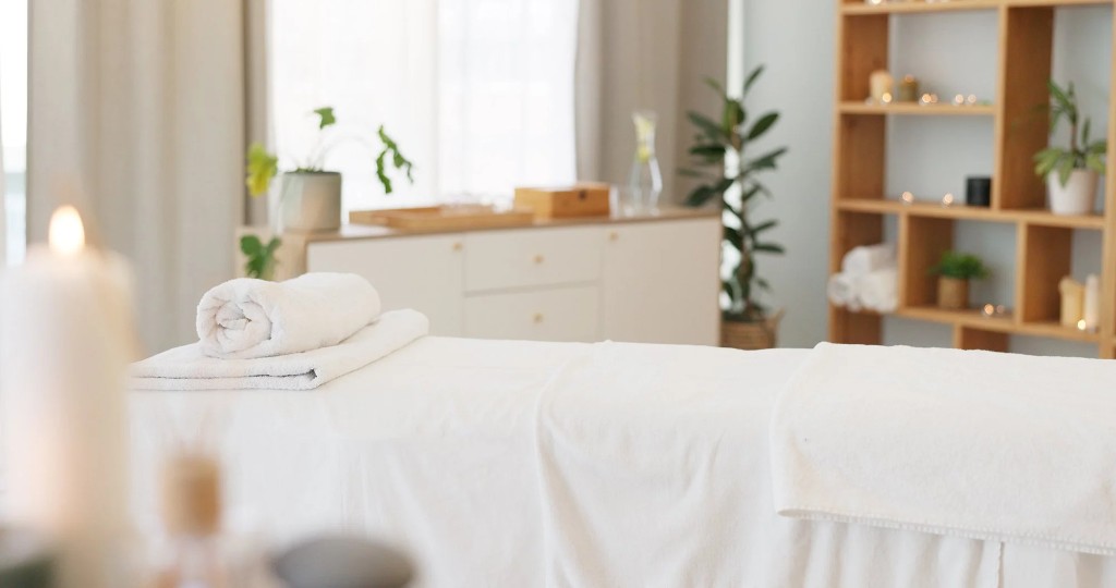 Massage table with white linens in a bright treatment room with candles and plants